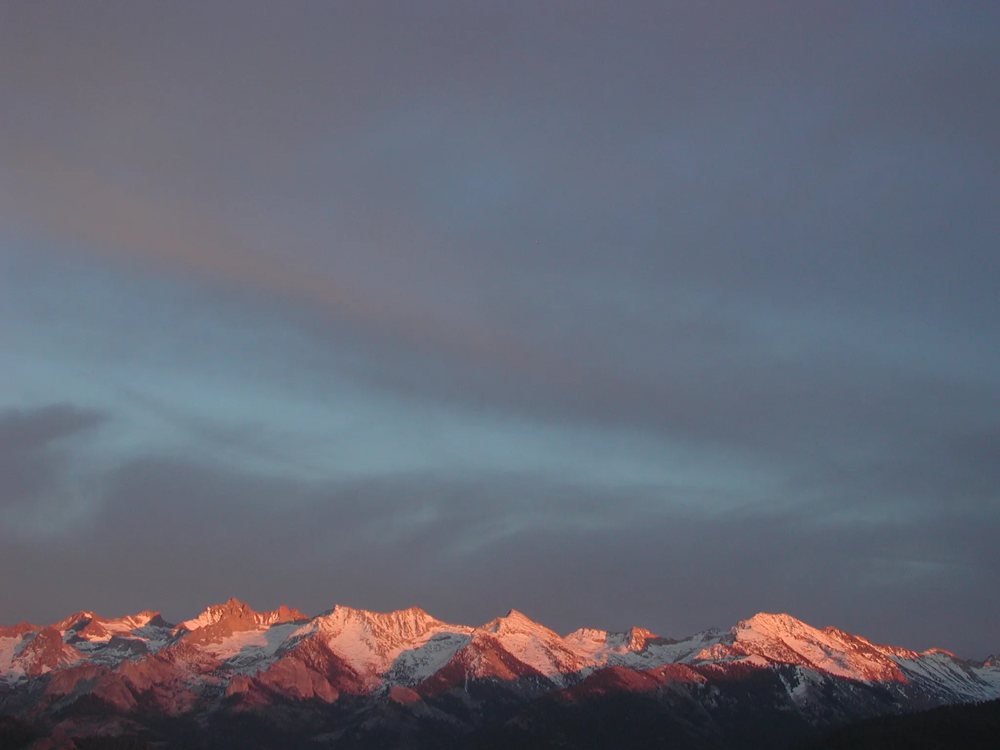 Sunset over a Sierra mountain range, sun just hitting the peaks against a bluegrey sky and mountainbase